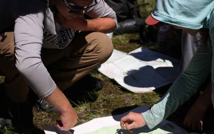 teens point to a map while navigating a backpacking expedition